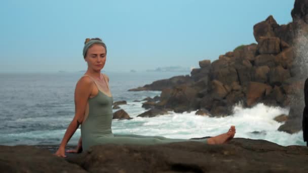 Спокойная женщина в сером сидит на скалистом побережье океана замедленной съемки — стоковое видео