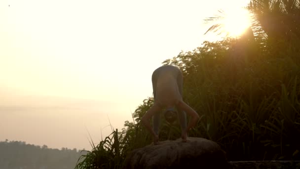 Lady practices yoga in uttanasana pose on rock slow motion — Stock Video