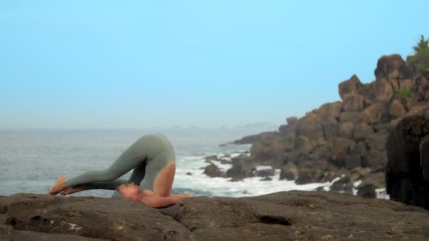 Женщина садится в карнапидасану на берегу моря замедленной съемки — стоковое видео