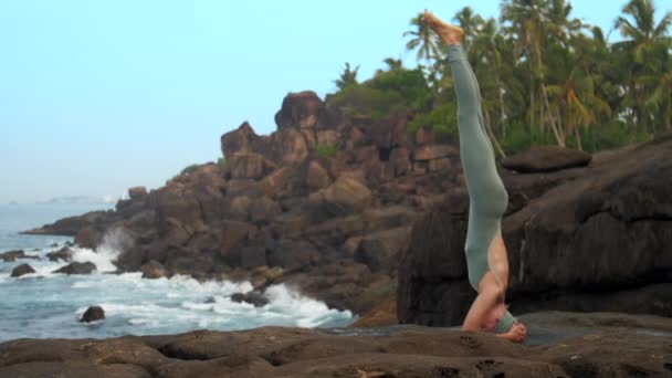 Ragazza in tuta grigia mostra sirsasana da oceano rallentatore — Video Stock