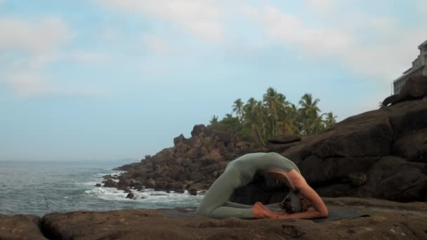 Девушка делает kapotasana позировать в спокойном океане замедленной съемки — стоковое видео