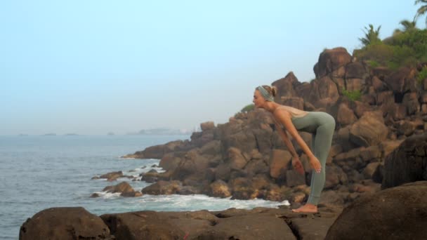 Грациозная девушка садится в uttanasana на камень замедленной съемки — стоковое видео