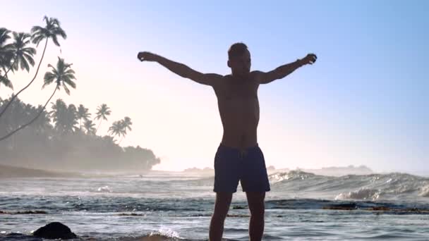 Desportista muscular levanta as mãos e pula na praia do oceano — Vídeo de Stock