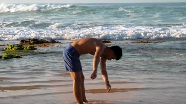 Atleta en pantalones cortos azules se extiende de pie en aguas poco profundas — Vídeos de Stock
