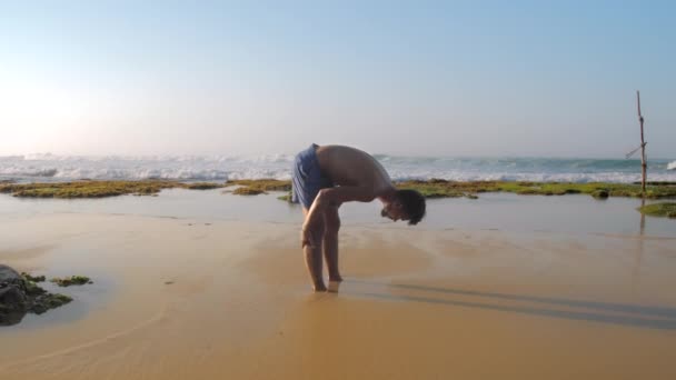 Guy stretches on sandy beach against foaming ocean waves — Stock Video