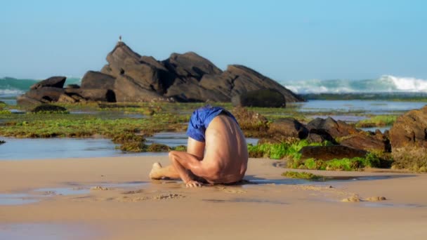 Muscular sportsman meditates in yoga pose on wet sand — Stock Video