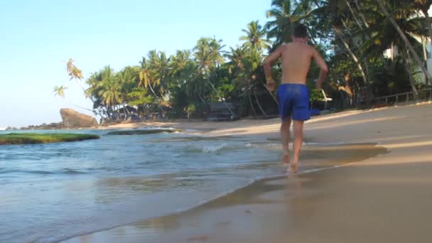 Mavi şort adam çalışır ve köpüklü okyanus dalgası woges — Stok video