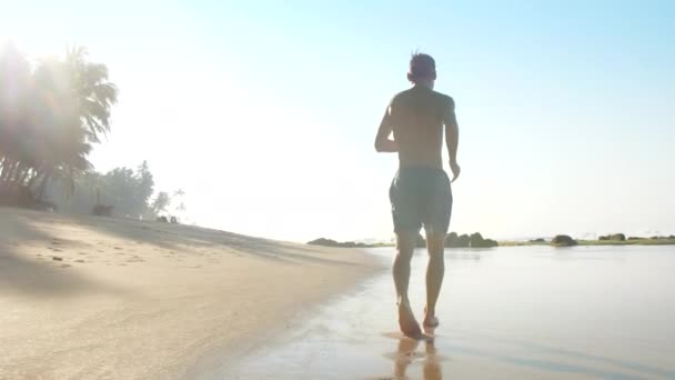 Güçlü atlet güneş tarafından aydınlatılmış okyanus kıyı şeridi yavaş boyunca çalışır — Stok video