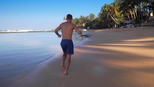 Hübscher Athlet läuft bei Übungen entlang der Meeresküste — Stockvideo