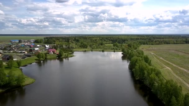 Мальовнича блакитна річка тече між маленьким селом і полем — стокове відео