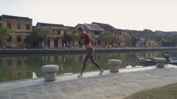 Flygvy ung kvinna gör morgon övningar vid floden — Stockvideo
