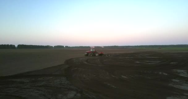 Luchtbeweging rond rode tractor werken in het veld in de avond — Stockvideo