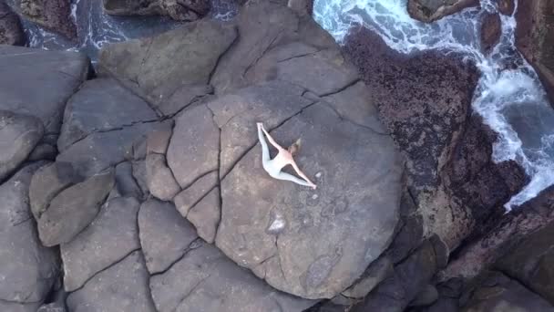 Chica estira las piernas acostado en gran piedra gris por la orilla del océano — Vídeo de stock
