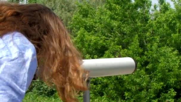 Брюнетка смотрит в городской телескоп в парке — стоковое видео
