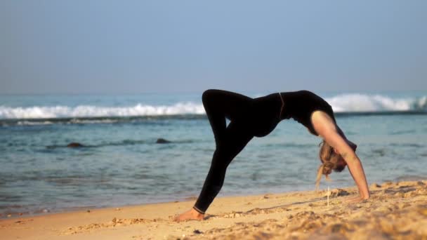 Chica en negro chándal hace yoga pose rueda con la pierna hacia arriba — Vídeo de stock