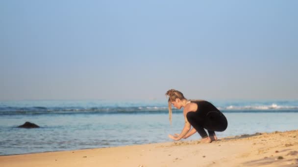 Girl with space buns practices yoga pose crow on sand beach — Stock Video