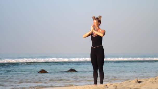 Vrouw met ruimte broodjes verandert yoga poses op het strand — Stockvideo