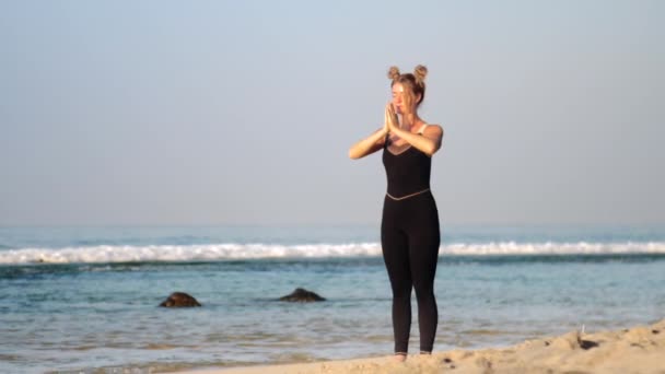 Female with space buns changes yoga poses on beach — Stock Video