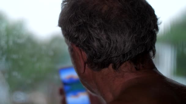 Ανώτερος πολίτης κοιτάζει το smartphone στέκεται στο παράθυρο — Αρχείο Βίντεο