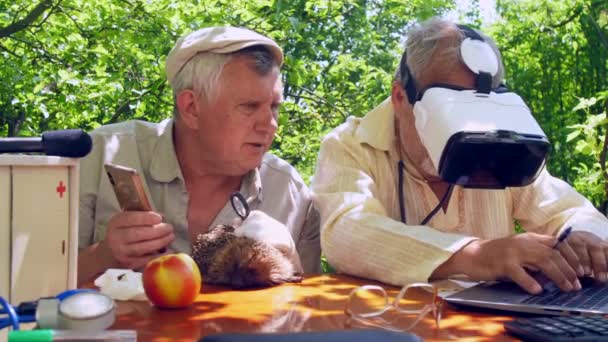 W wieku mężczyzna ze smartfonem trzyma jeża i rozmawia z seniorami — Wideo stockowe