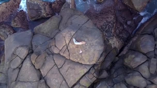 Гнучка жінка лежить на величезному сірому камені бірюзовим океаном — стокове відео