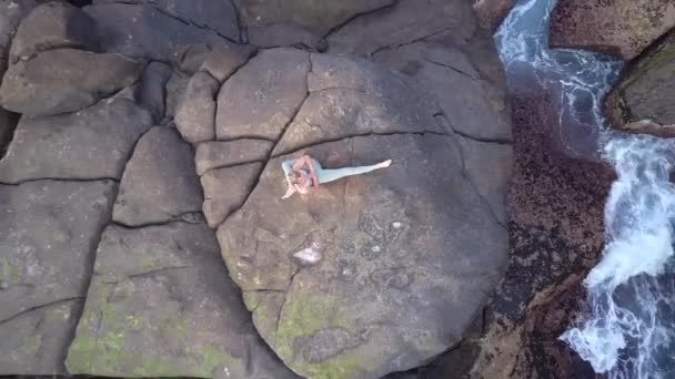 Стройная женщина сидит в современном положении йоги на большом сером камне — стоковое видео