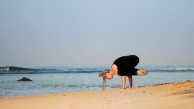 sarışın kadın kumlu okyanus kıyısında yoga poz karga meditasyon