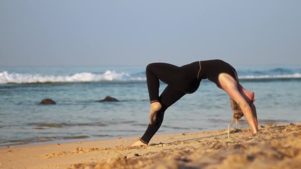 Ragazza bionda mostra avanzato yoga posa ruota sulla spiaggia — Video Stock