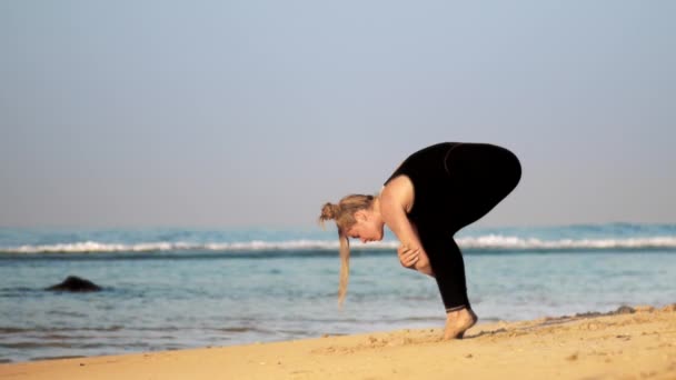 Sportieve meisje doet voorwaarts vouwen yoga pose op Ocean Beach — Stockvideo