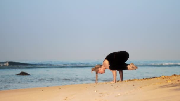 Blond woman meditates in yoga pose crow on sandy ocean coast — Stock Video