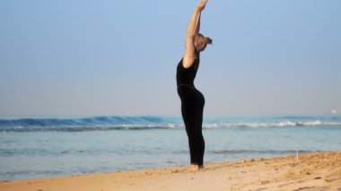 eşofmanlı genç kadın okyanus sahilinde pilates yapıyor