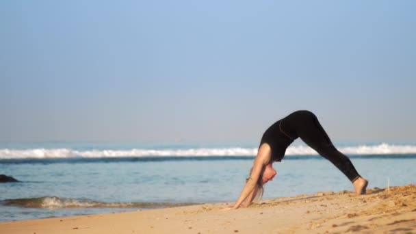 Menina de cabelos justas em traje de treino faz pilates na praia iluminada pelo sol — Vídeo de Stock