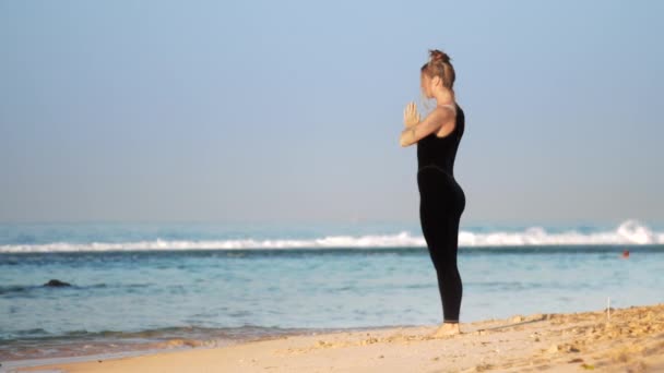 Mooie dame in Sportswear mediteert op zonsopgang op het strand — Stockvideo