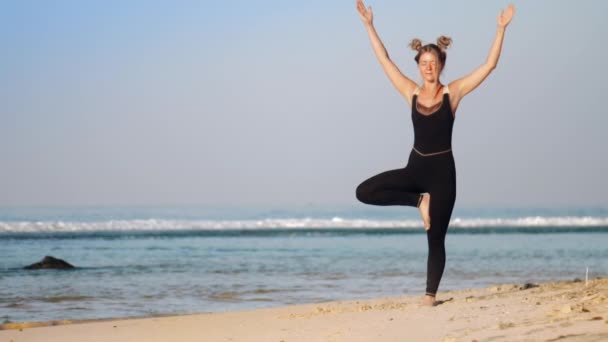 Blonde fille aux cheveux en survêtement noir ne yoga pose arbre — Video