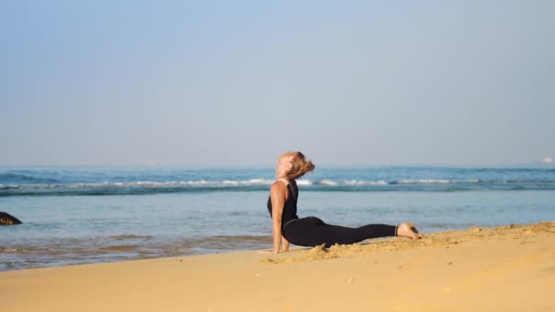 Blondes Mädchen im schwarzen Trainingsanzug meditiert in Yoga-Pose Kobra — Stockvideo