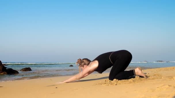 Barefoot girl in black tracksuit exercises on sandy beach — Stock Video