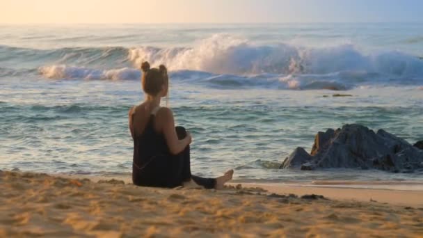 Slanke dame in zwart mediteert op zandstrand door oceaan golven — Stockvideo