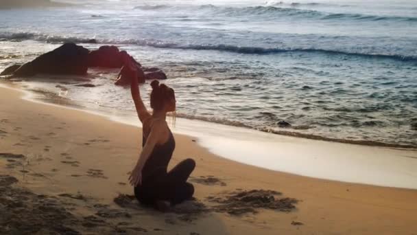 Захоплююча леді в чорному костюмі в позі йоги біля океану — стокове відео