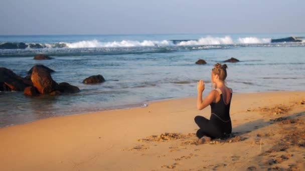 Young blond woman in black tracksuit meditates in yoga pose — Stock Video