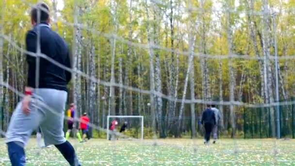 Vista através de portão net caras jogar futebol no parque de outono — Vídeo de Stock