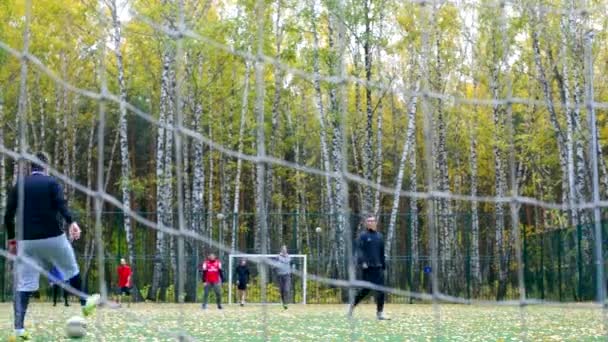 Vista através de portão net em caras que jogam futebol no campo — Vídeo de Stock