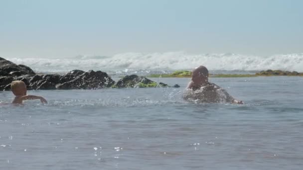 Apa és kisfiú játszik fröccsenő víz nyugodt óceán — Stock videók