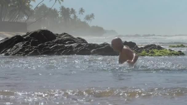 Hombre feliz salpica el agua en las rocas viejas en el resort cámara lenta — Vídeo de stock