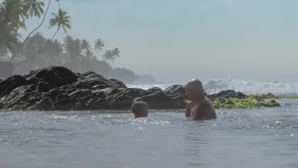 Küçük çocuk kayalara okyanus suyu sıçrayan baba ile oynar — Stok video