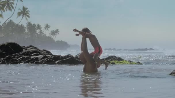 Забавный мальчик забирается на плечи отца и прыгает в море на скалах — стоковое видео