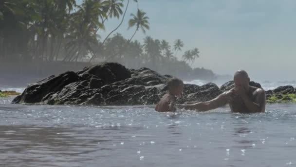 父亲与小男孩在温暖的海水中对棕榈树玩耍 — 图库视频影像