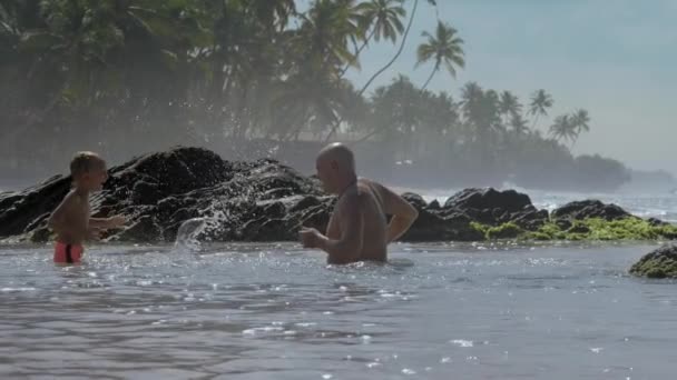 Мальчик и папа плескаются водой, играя в океанской воде на курорте — стоковое видео