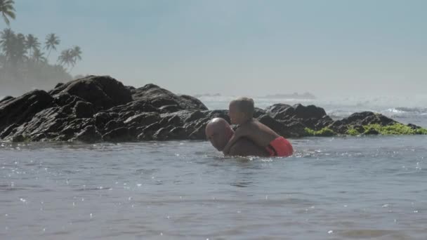 Papi nada con el niño en la espalda en grandes piedras en el mar — Vídeos de Stock