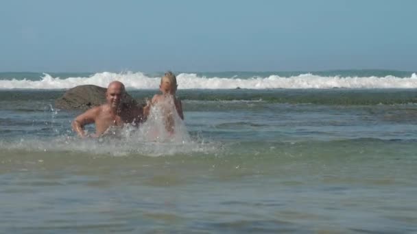 Pai e filho jogar salpicando água do oceano claro contra onda — Vídeo de Stock