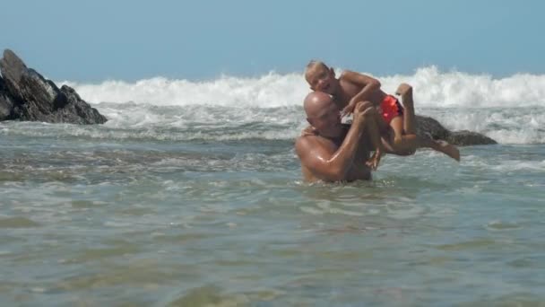 Ο μπαμπάς με το γιο στον ώμο στηρίζεται σε γαλάζιο νερό του ωκεανού — Αρχείο Βίντεο